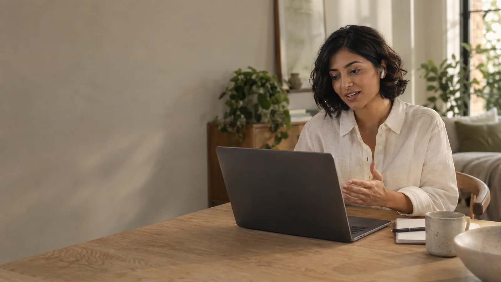 Woman speaking to a voice assistant at her laptop in a warm home workspace.