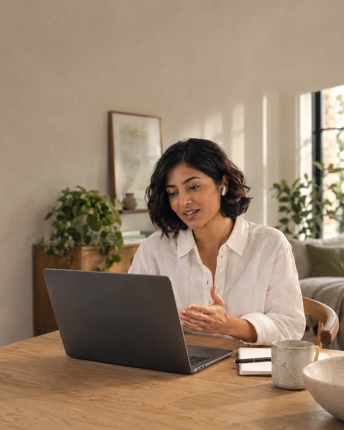 Woman speaking to a voice assistant at her laptop in a warm home workspace.
